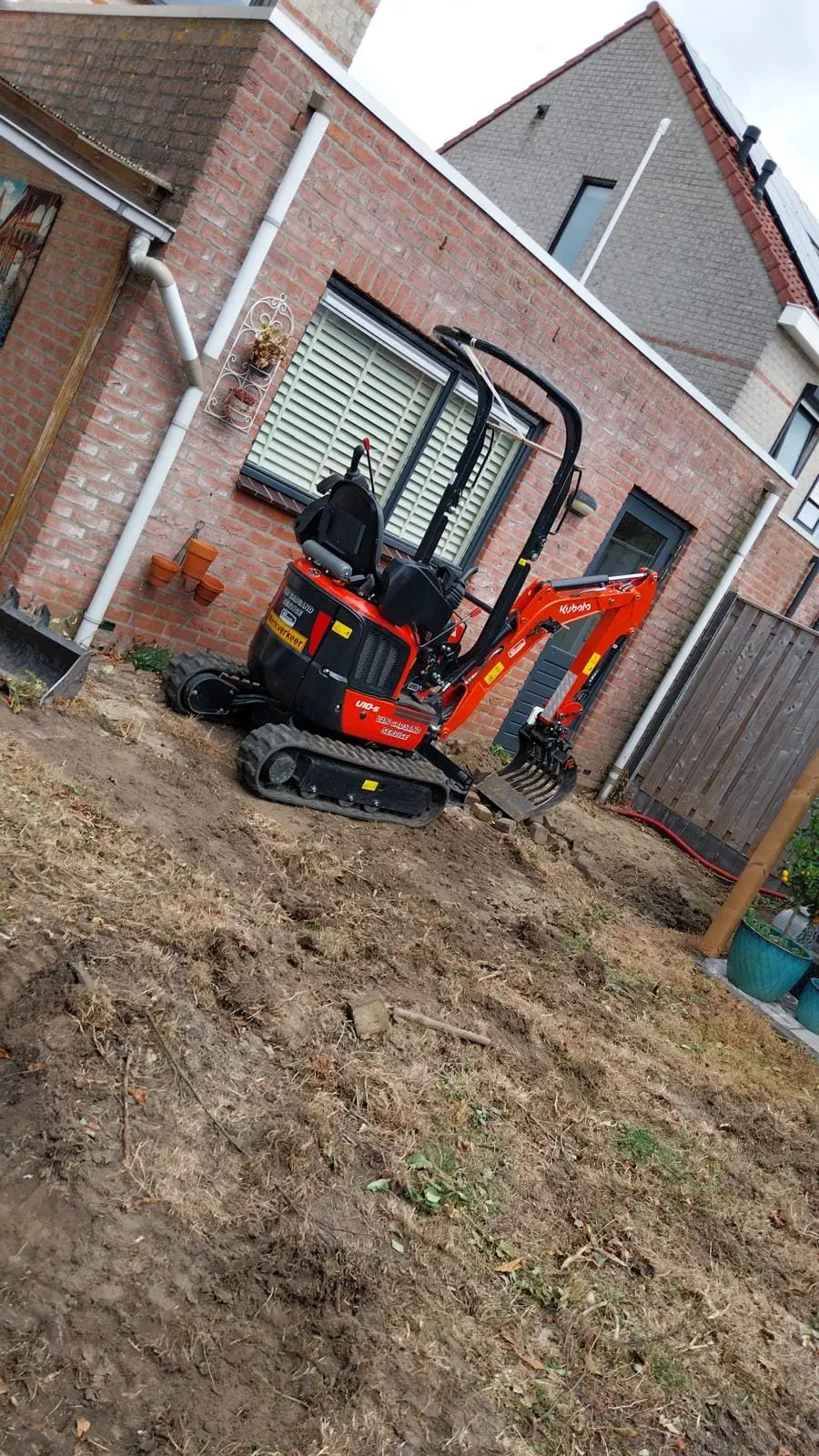Minikraan graaft de tuin uit langs de woning