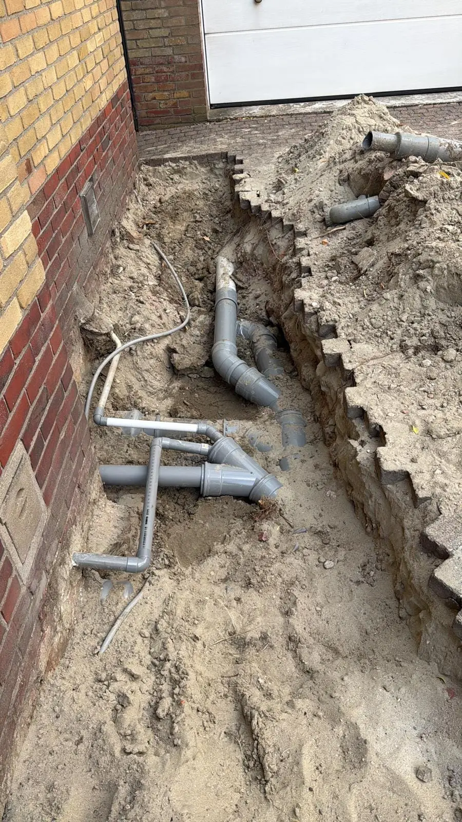 Nieuwe rioolbuis in een uitgegraven sleuf naast de woning